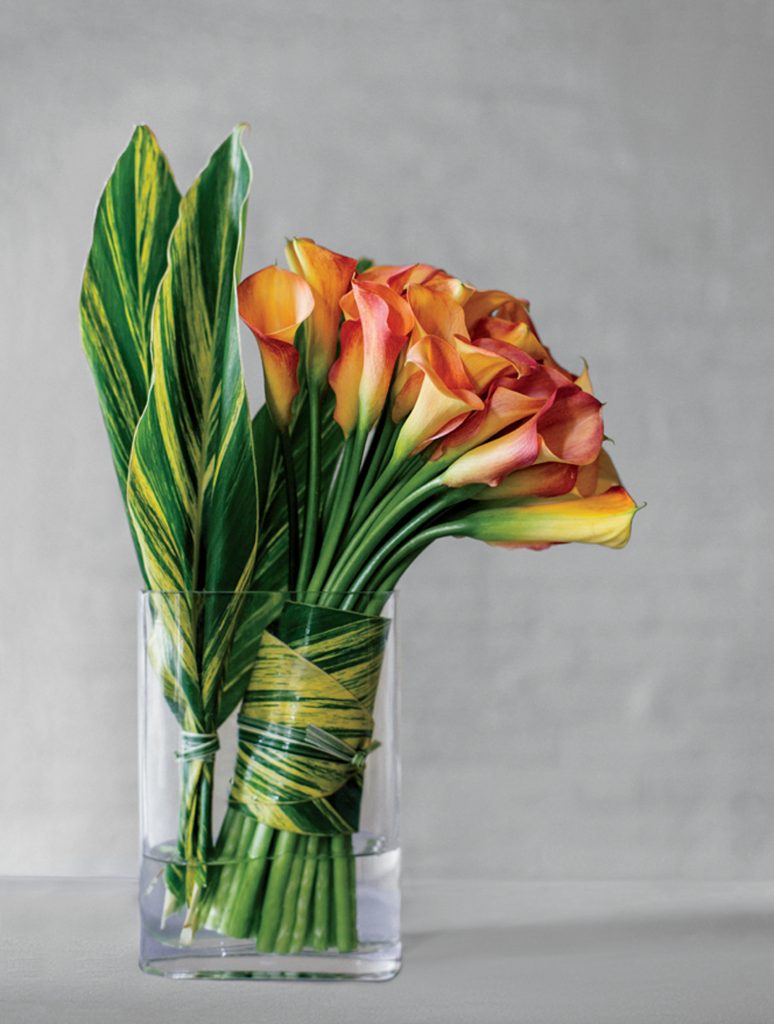 Orange calla lilies and yellow and green ginger leaves are combined in a simple but dramatic arrangement