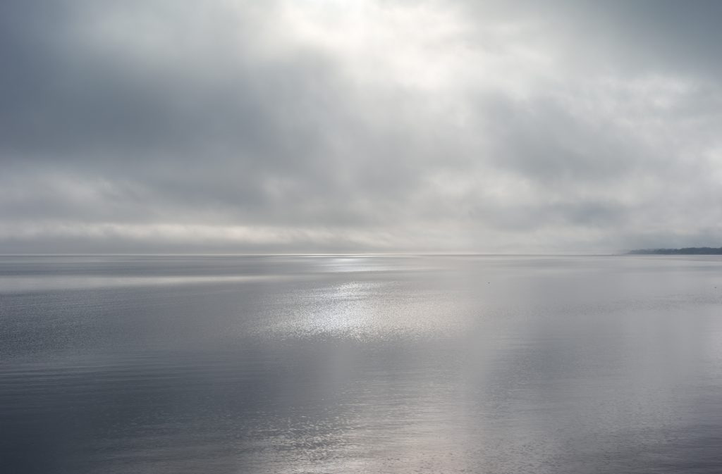 Shot on a beach at the Eastern tip of the North Fork in Orient, New York, Orient Fog II shows the ocean reflecting the grey sky above. 