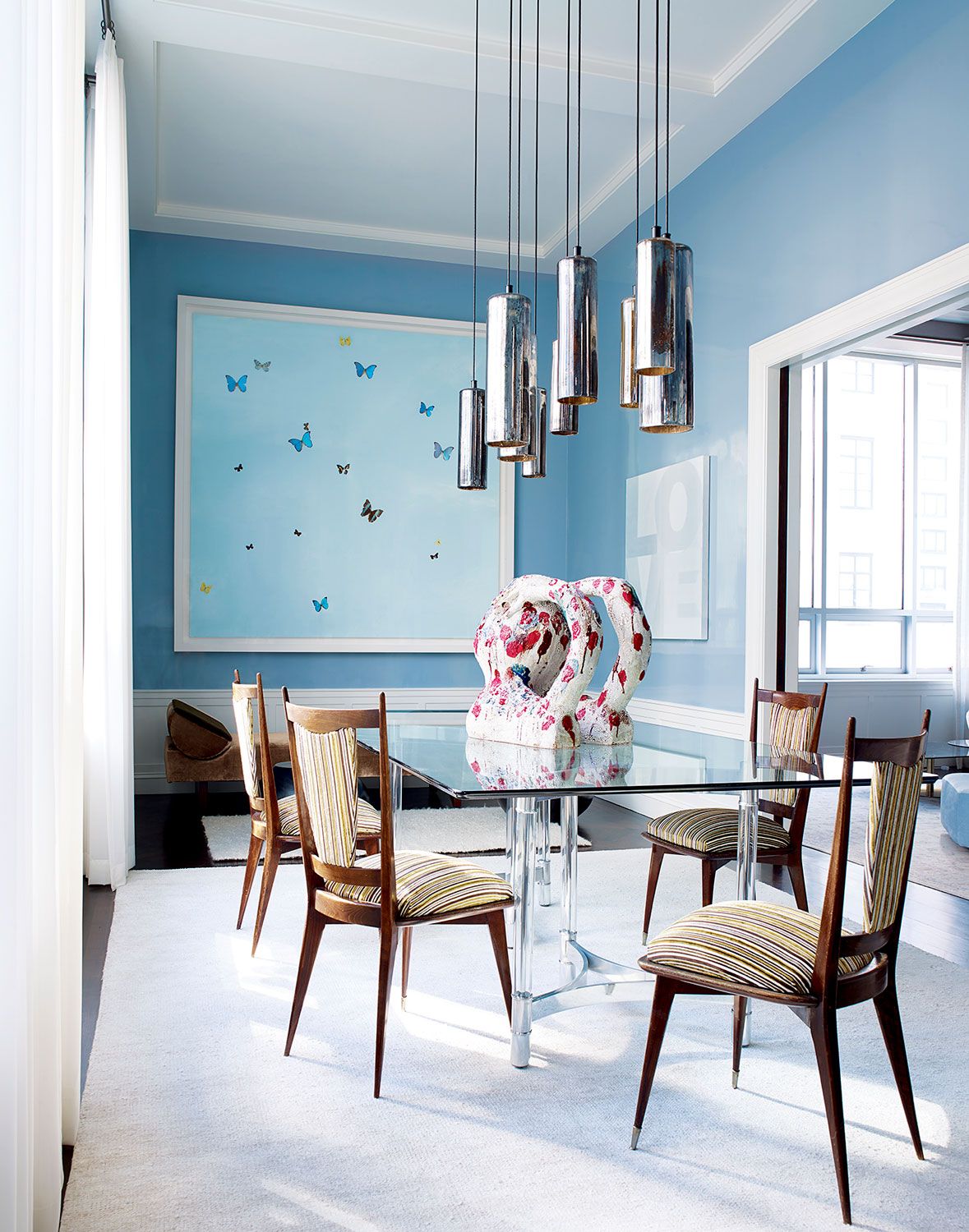 Italian chairs from the 1960s surround the vintage dining table, and the vintage mercury-glass canister pendants are by Gregory Rogan; the sculpture is by William J. O’Brien; a butterfly painting by Damien Hirst hangs above a Kevin Walz daybed by Ralph Pucci.